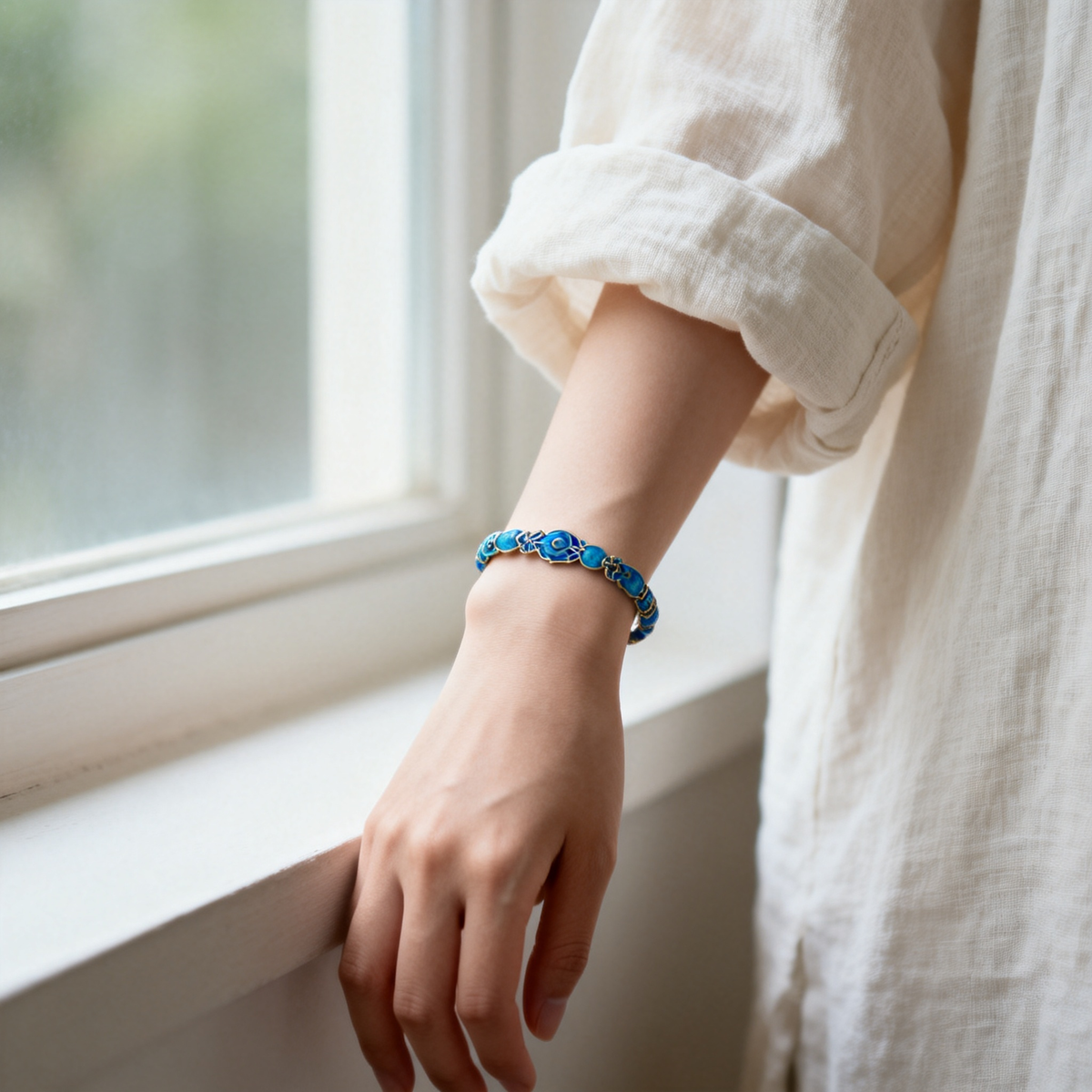 Woman's wrist wearing handmade cloisonne enamel bracelet, neutral sleeve