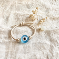 Handmade evil eye bracelet with blue glass charm on linen, dried flowers beside